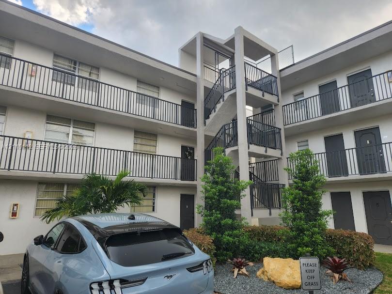 Multi-story building exterior featuring a central concrete staircase, metal railings, and integrated landscaping with ornamental shrubs and stone accents