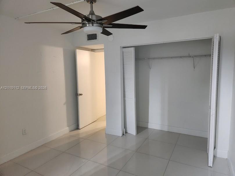 Large-format neutral tile flooring, multi-blade ceiling fan with integrated lighting, and closet with louvered bi-fold doors