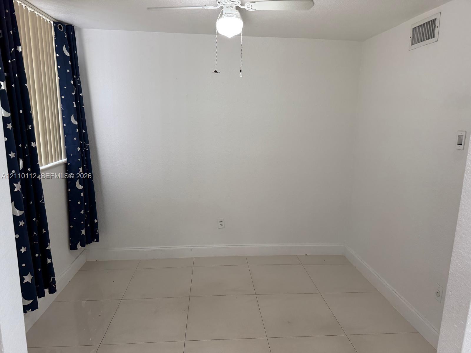 Room featuring large-format tile flooring, vertical blinds, and a central ceiling fan with an integrated light fixture