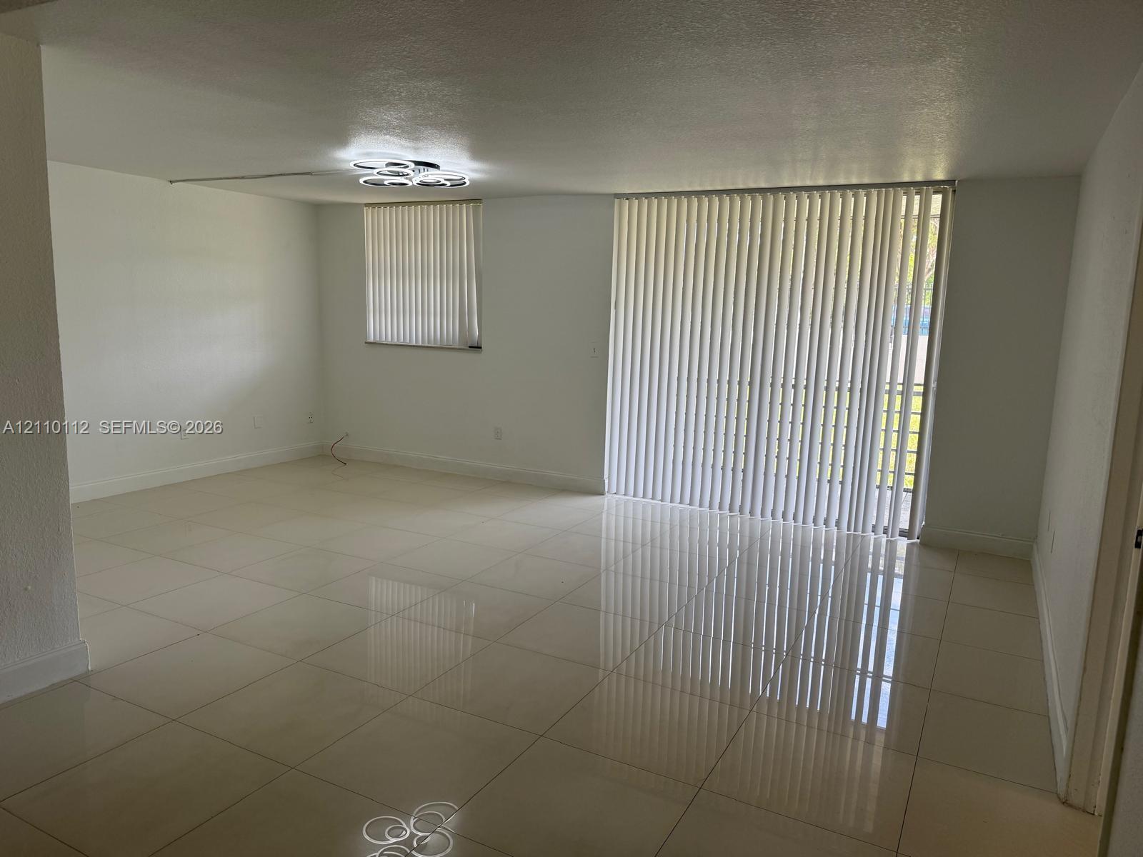 Large-format tile flooring, recessed flush-mount geometric ceiling lighting, and vertical window blinds