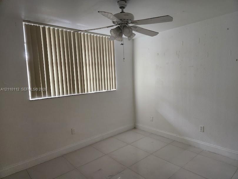 Room featuring white tile flooring, ceiling fan with integrated light fixture, and vertical window blinds