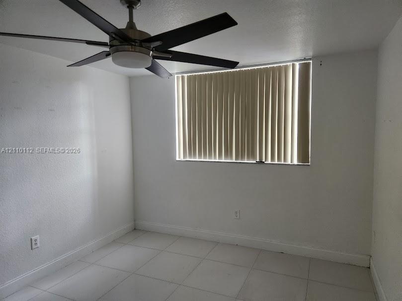 Room featuring large-format ceramic tile flooring, a multi-blade ceiling fan with integrated lighting, and vertical window blinds