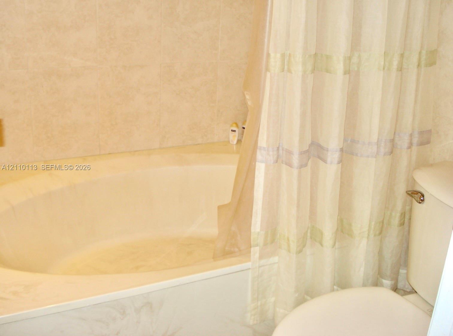 Oval soaking tub with a porcelain finish, accompanied by neutral-toned wall tile surround and a standard toilet