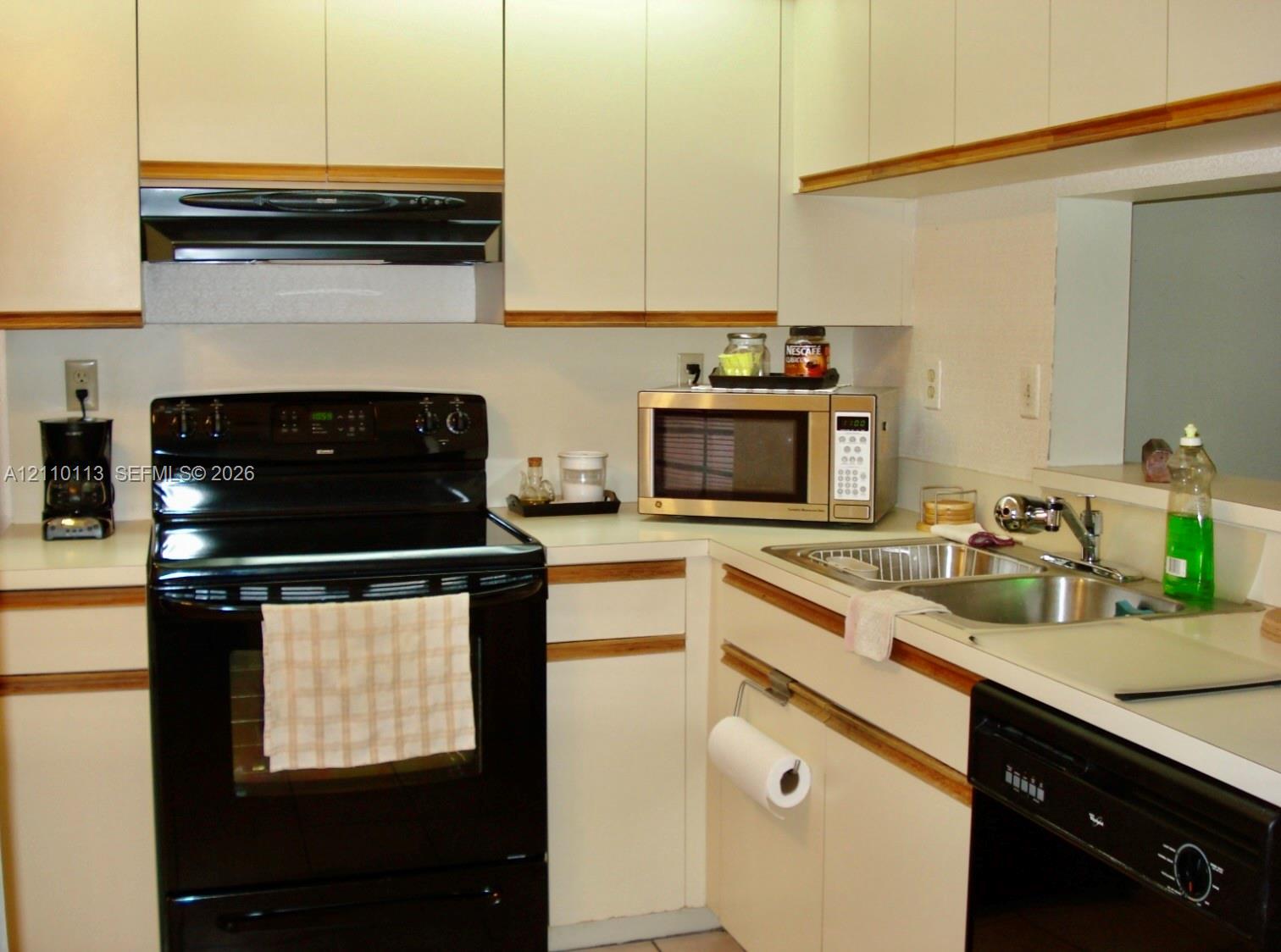 Kitchen featuring flat-panel cabinetry with wood trim, contrasting black appliances, a double-basin stainless steel sink, and solid-surface countertops