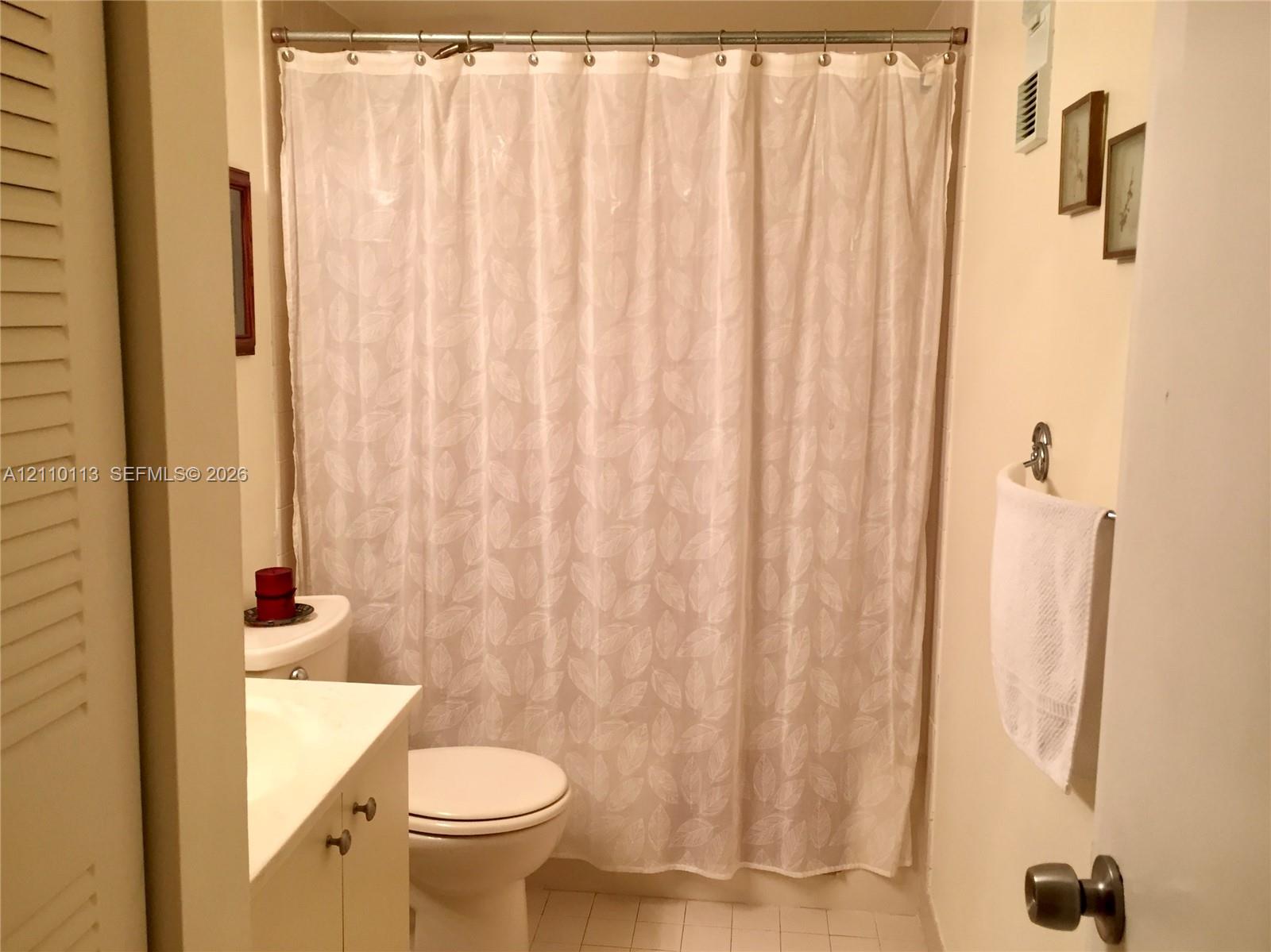 Bathroom featuring a white vanity cabinet, ceramic tile flooring, and a tub-shower combination with a metal curtain rod and hardware