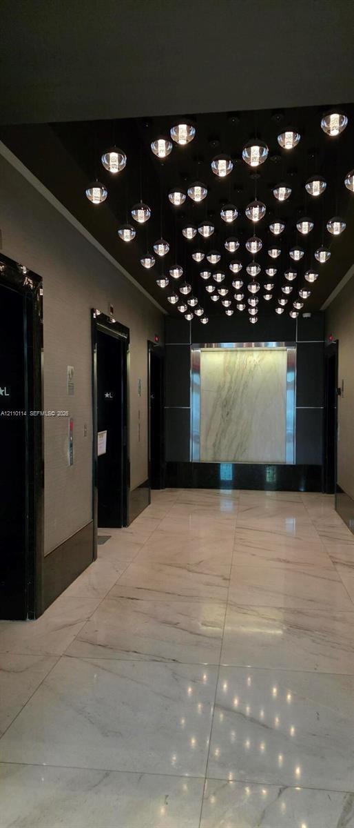Grand lobby featuring large-format polished stone flooring, custom multi-pendant ceiling lighting, stone wall accent paneling, and high-gloss door frames