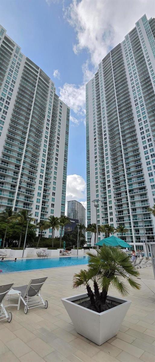 High-rise towers featuring floor-to-ceiling glass paneling and private balconies, complemented by an outdoor swimming pool, paved sundeck, and palm tree landscaping