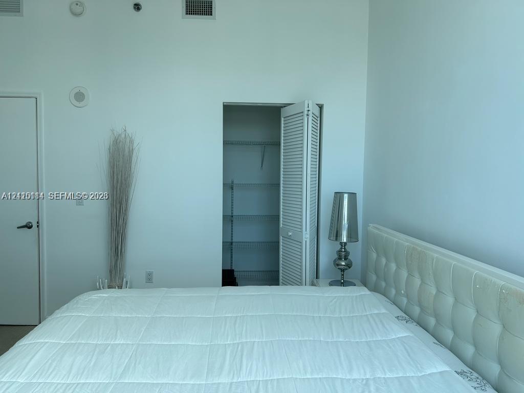 High ceilings featuring integrated ceiling-mounted speakers and a walk-in closet with built-in shelving and louvered folding doors