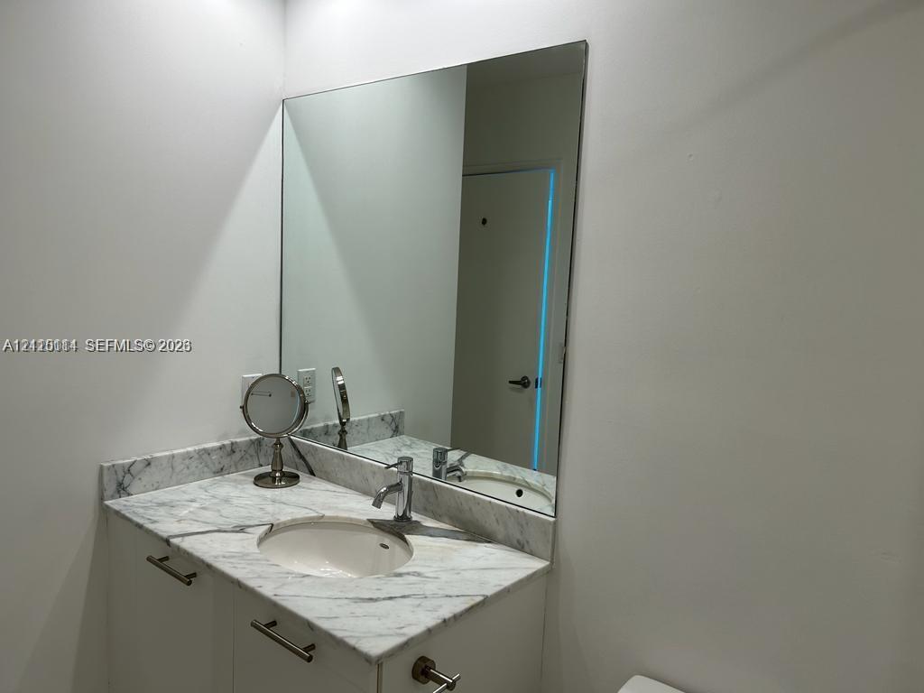 Vanity featuring a stone-top counter, undermount sink, metal faucet, and built-in cabinetry with metal pulls, complemented by a large, wall-mounted mirror