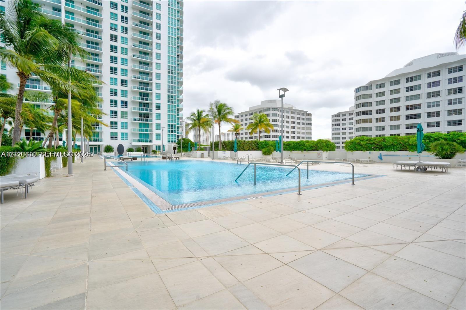 In-ground swimming pool featuring tile coping, metal handrails, and a paved deck surface
