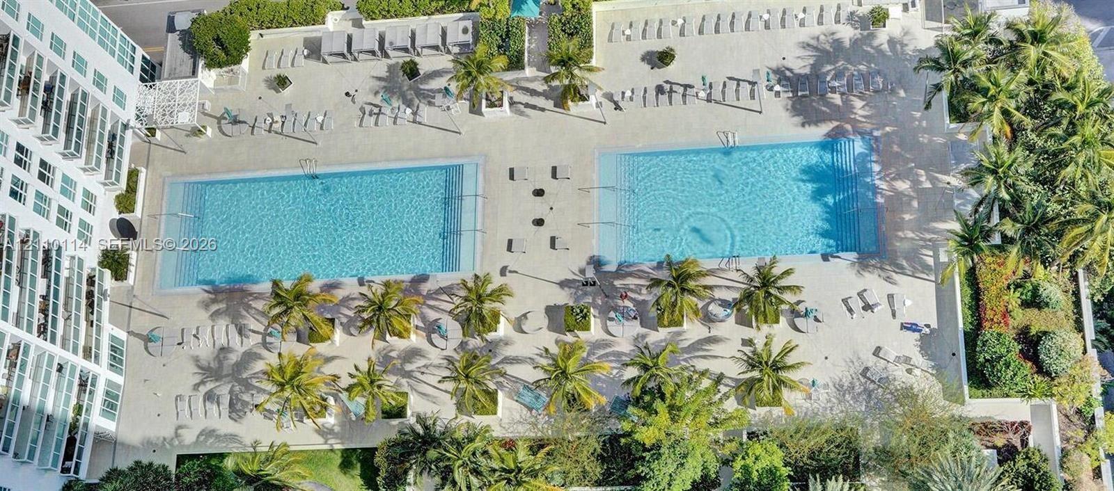 Dual swimming pools featuring expansive stone-paved decking, integrated landscaping, and numerous palm trees