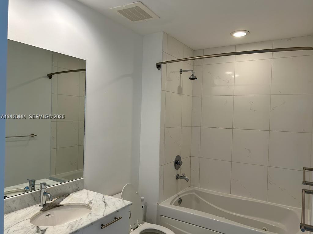 Bathroom featuring a vanity with a light-toned stone countertop, integrated sink, wall-mounted mirror, tub-shower combination with full-height tile surround, and metallic hardware