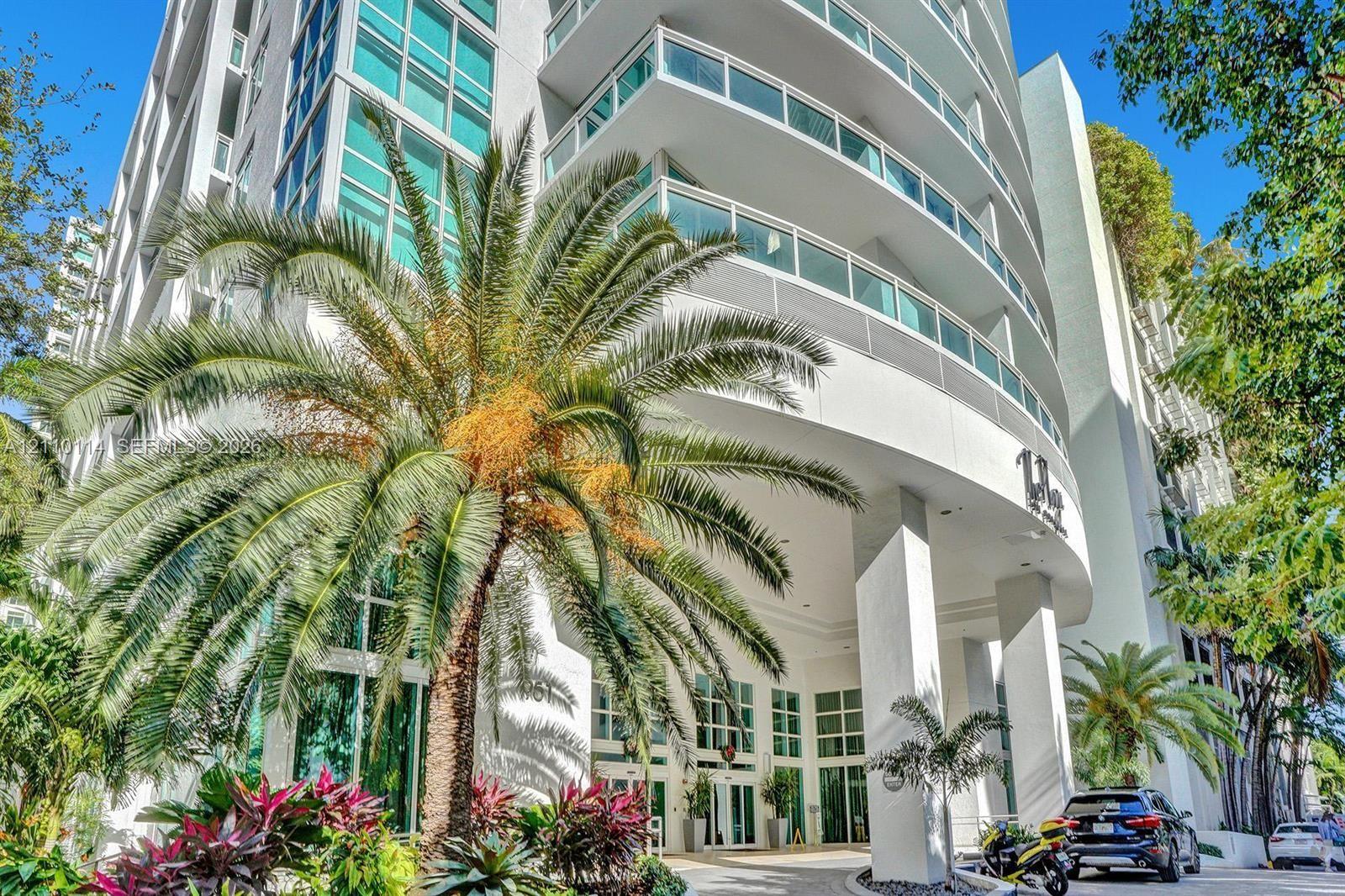 Modern high-rise exterior featuring curved balconies, floor-to-ceiling glass windows, concrete structure, and ground-level landscaping