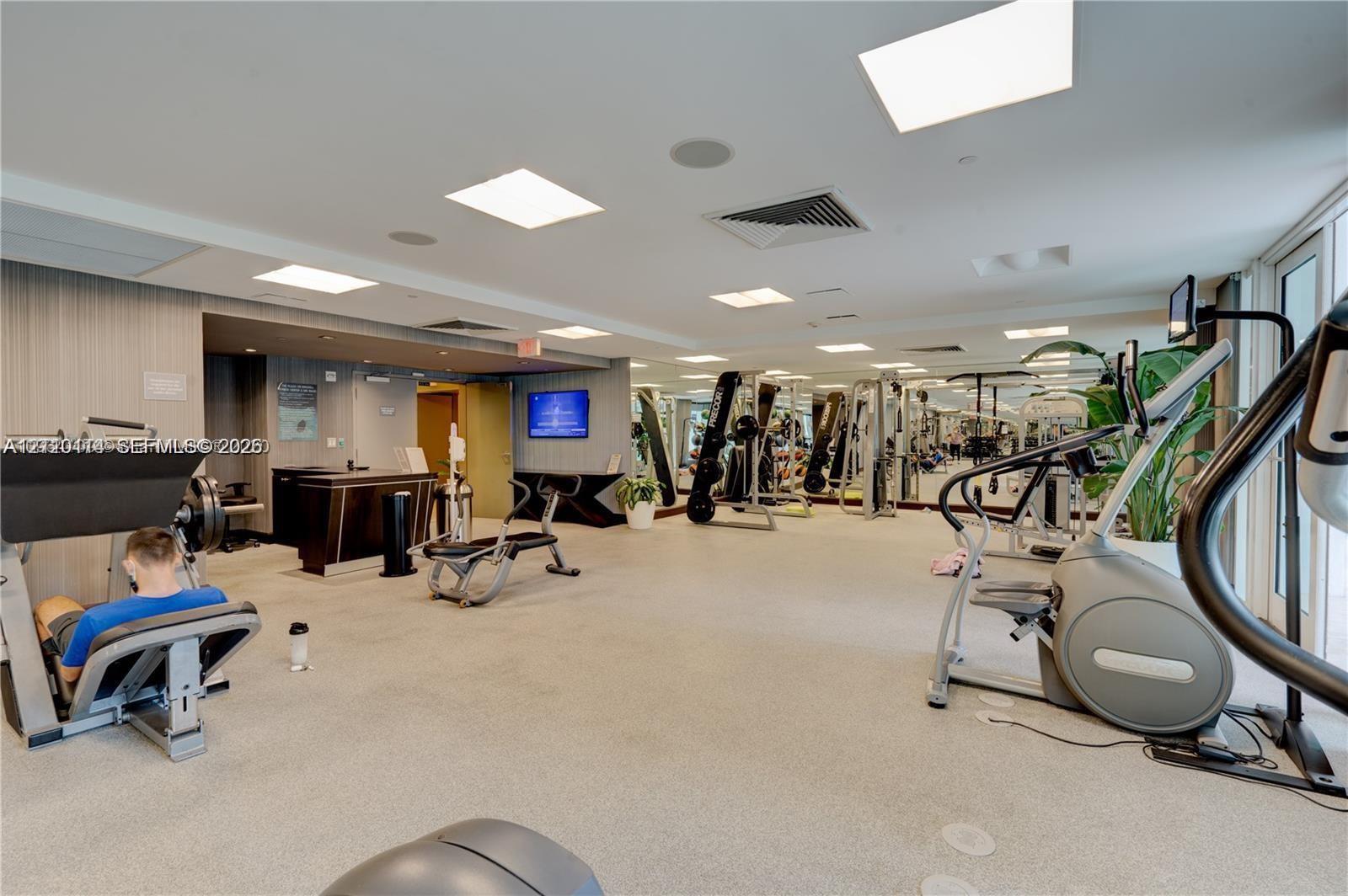 Fitness center featuring neutral carpeting, recessed lighting, expansive wall mirrors, and built-in reception cabinetry