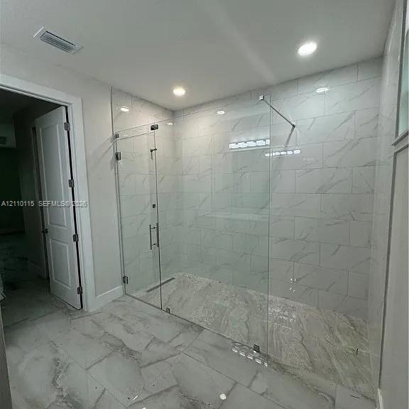Walk-in shower featuring a frameless glass enclosure, large-format tile wall surround, linear floor drain, and polished stone-finish floor tile