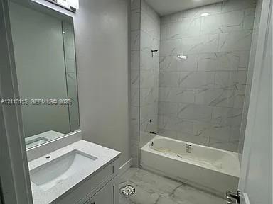 Full bathroom featuring a white vanity with a rectangular sink, quartz countertop, wall-mounted mirror, and a tub enclosure with full-height stone-patterned tile surround