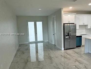 Large-format polished tile flooring, white shaker-style cabinetry, stainless steel French-door refrigerator, and glass-paneled double doors