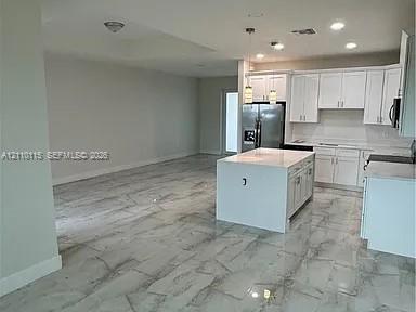 Kitchen featuring white cabinetry, center island with stone-finish countertop, stainless steel refrigerator, and large-format tile flooring