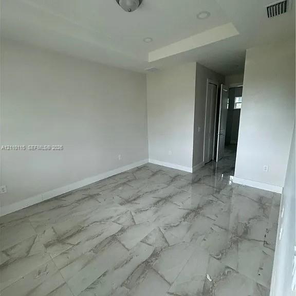 Interior room featuring large-format stone-finish tile flooring, recessed ceiling lighting, and a tray ceiling architectural detail