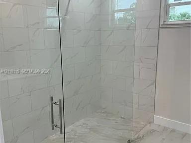 Walk-in shower featuring floor-to-ceiling large-format tile with veining, frameless glass enclosure, metallic hardware, and matching tile flooring