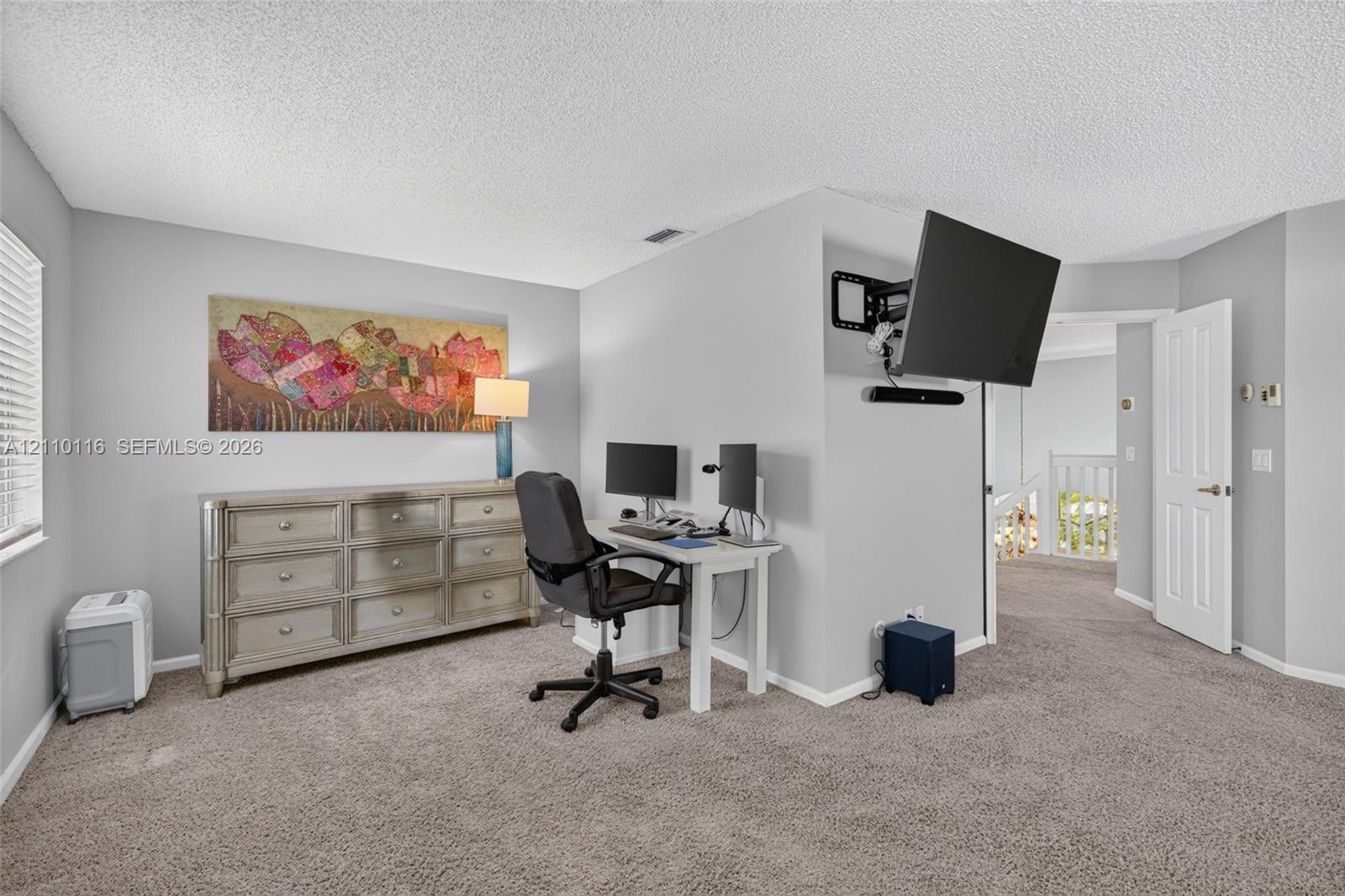 Neutral-toned wall paint, wall-mounted television bracket, carpeted flooring, and a multi-panel interior door