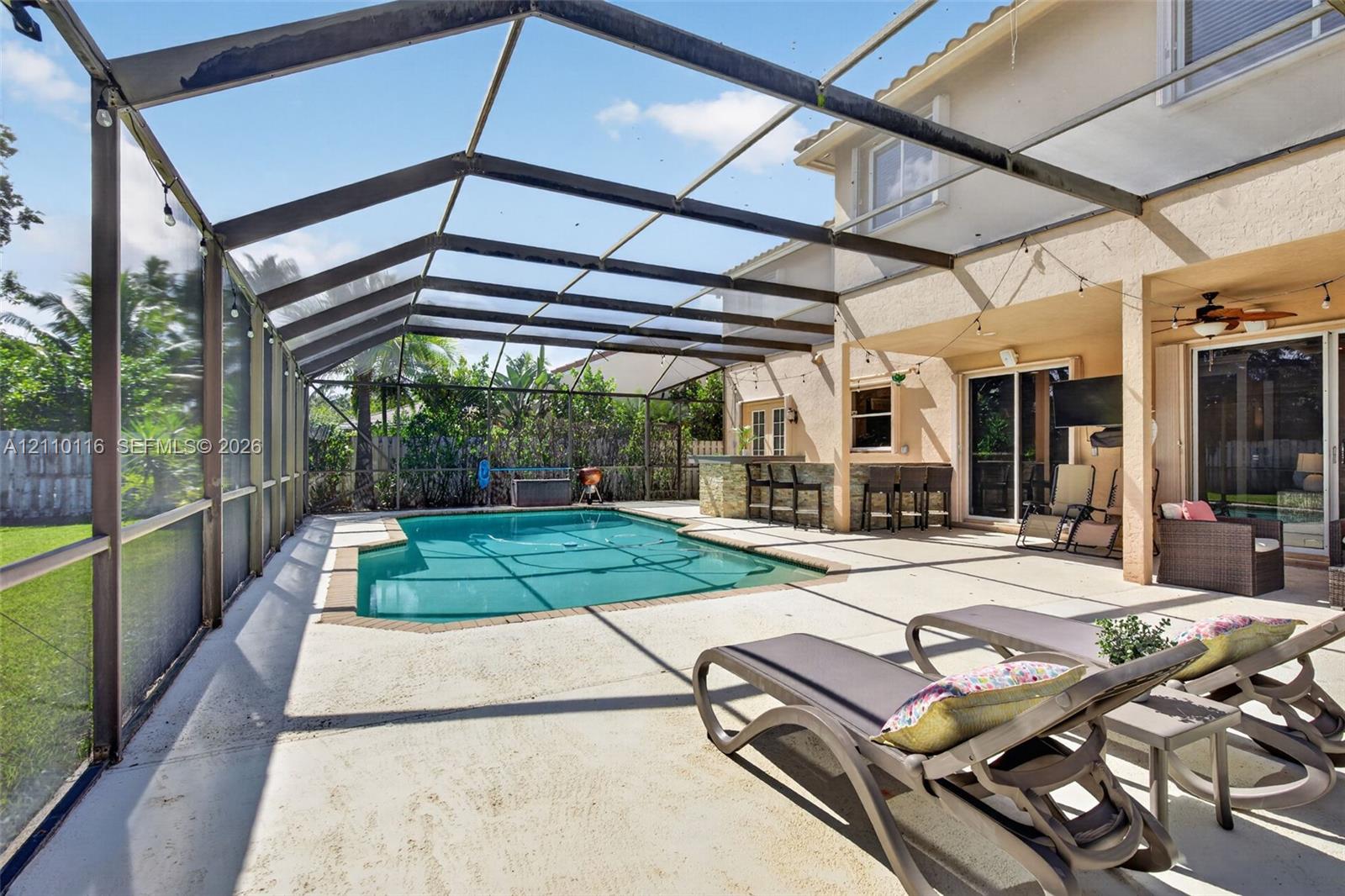 Screen-enclosed patio featuring a swimming pool, concrete pool deck, and a built-in outdoor bar with stone-finish siding