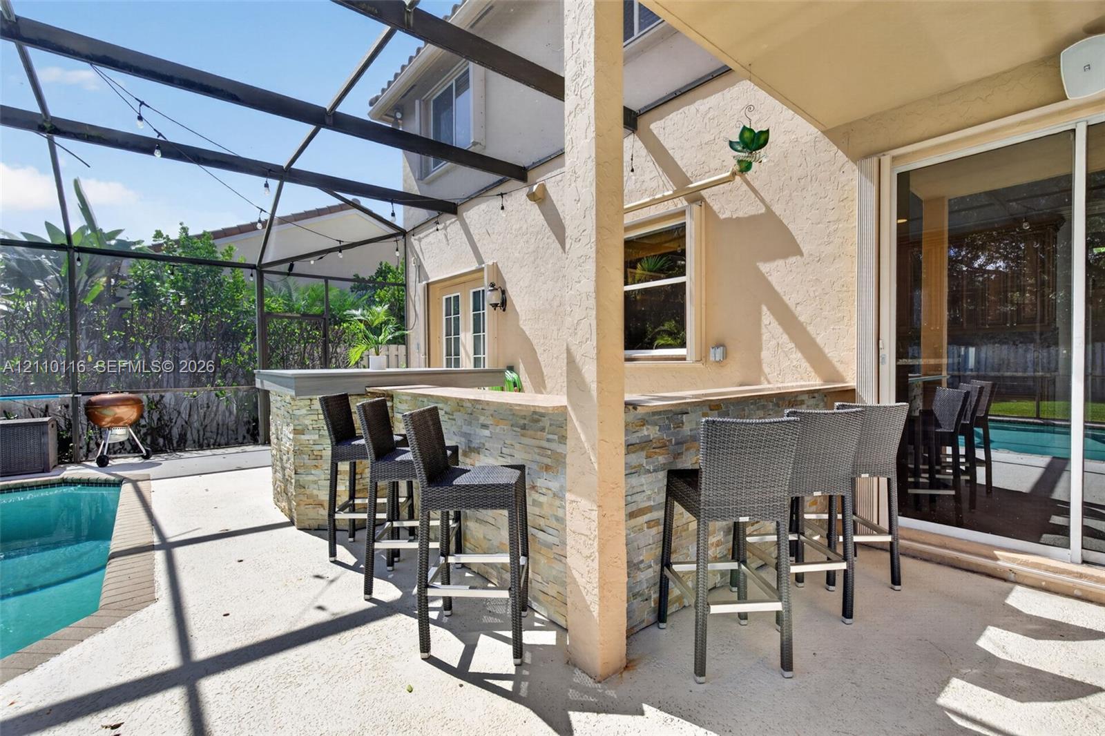 Screened-in patio featuring a stone-clad outdoor bar, built-in swimming pool, and sliding glass door access