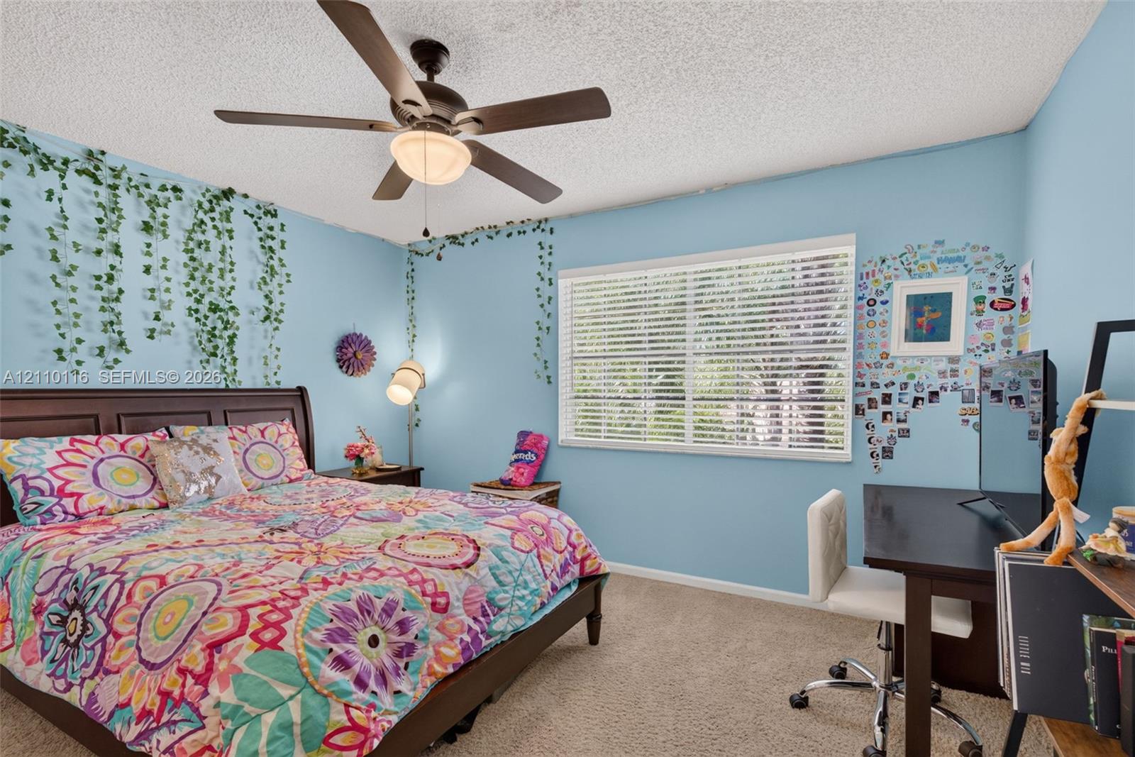 Neutral carpeted flooring, large window with horizontal blinds, and ceiling fan with integrated lighting