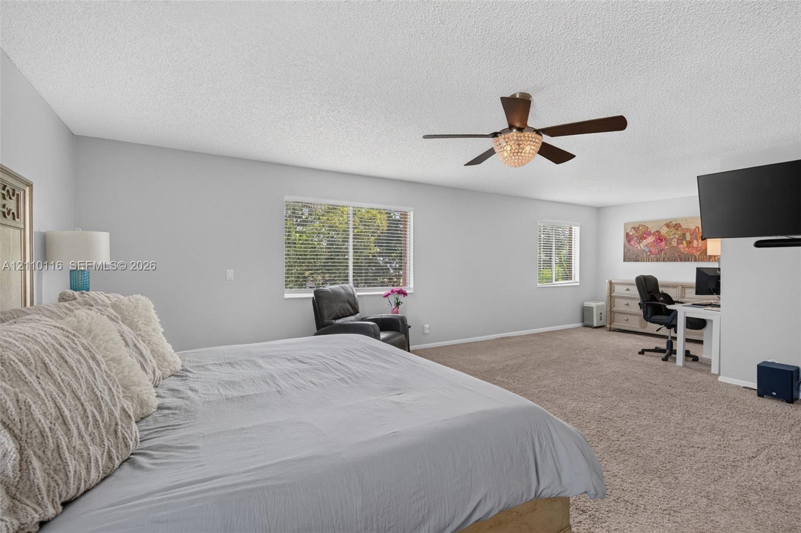 Spacious room featuring neutral wall tones, wall-to-wall carpeting, multiple windows, and a central ceiling fan with integrated light fixture