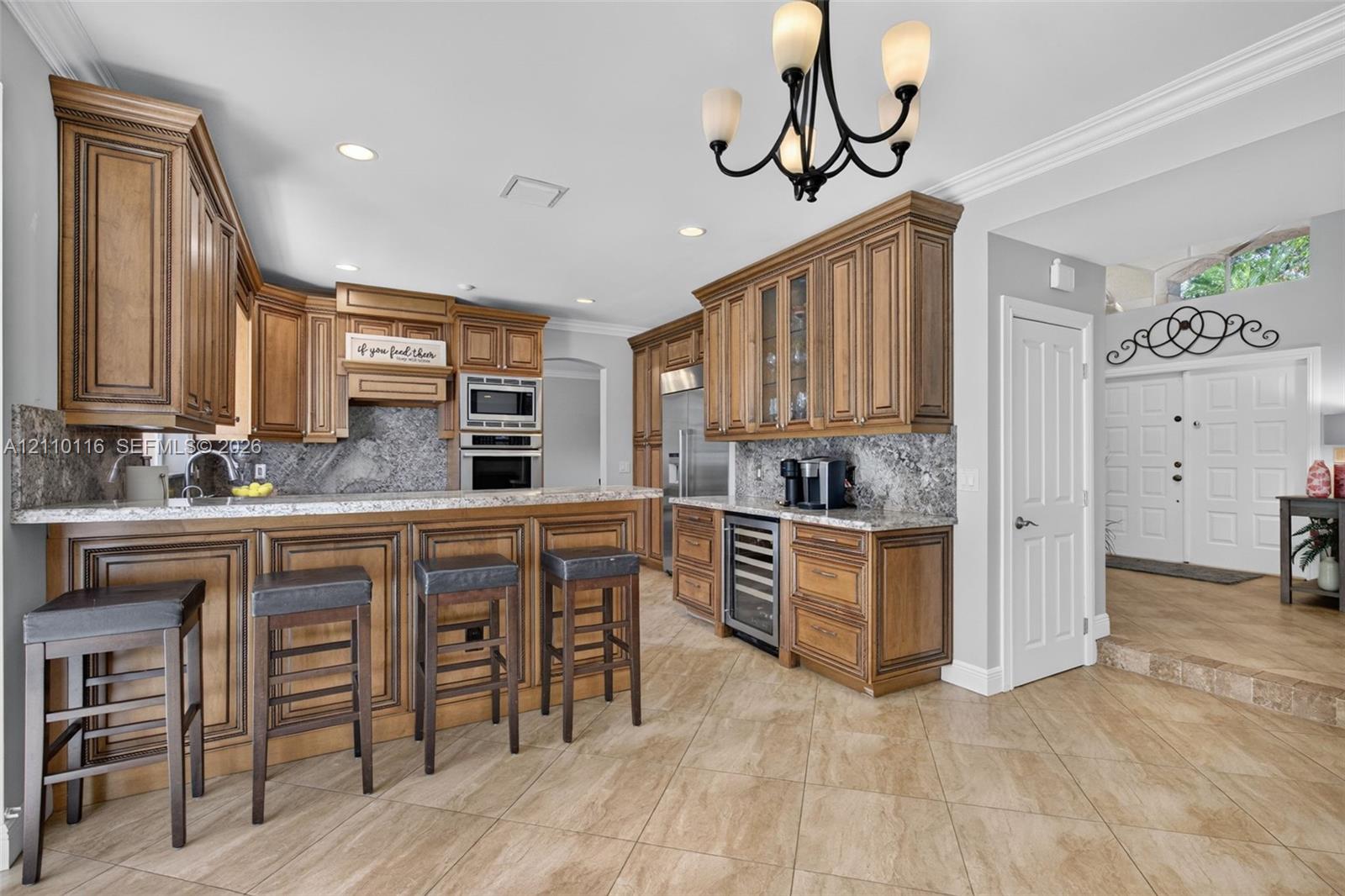 Kitchen featuring custom raised-panel wood cabinetry, stone countertops, integrated beverage refrigerator, recessed lighting, and a multi-arm chandelier