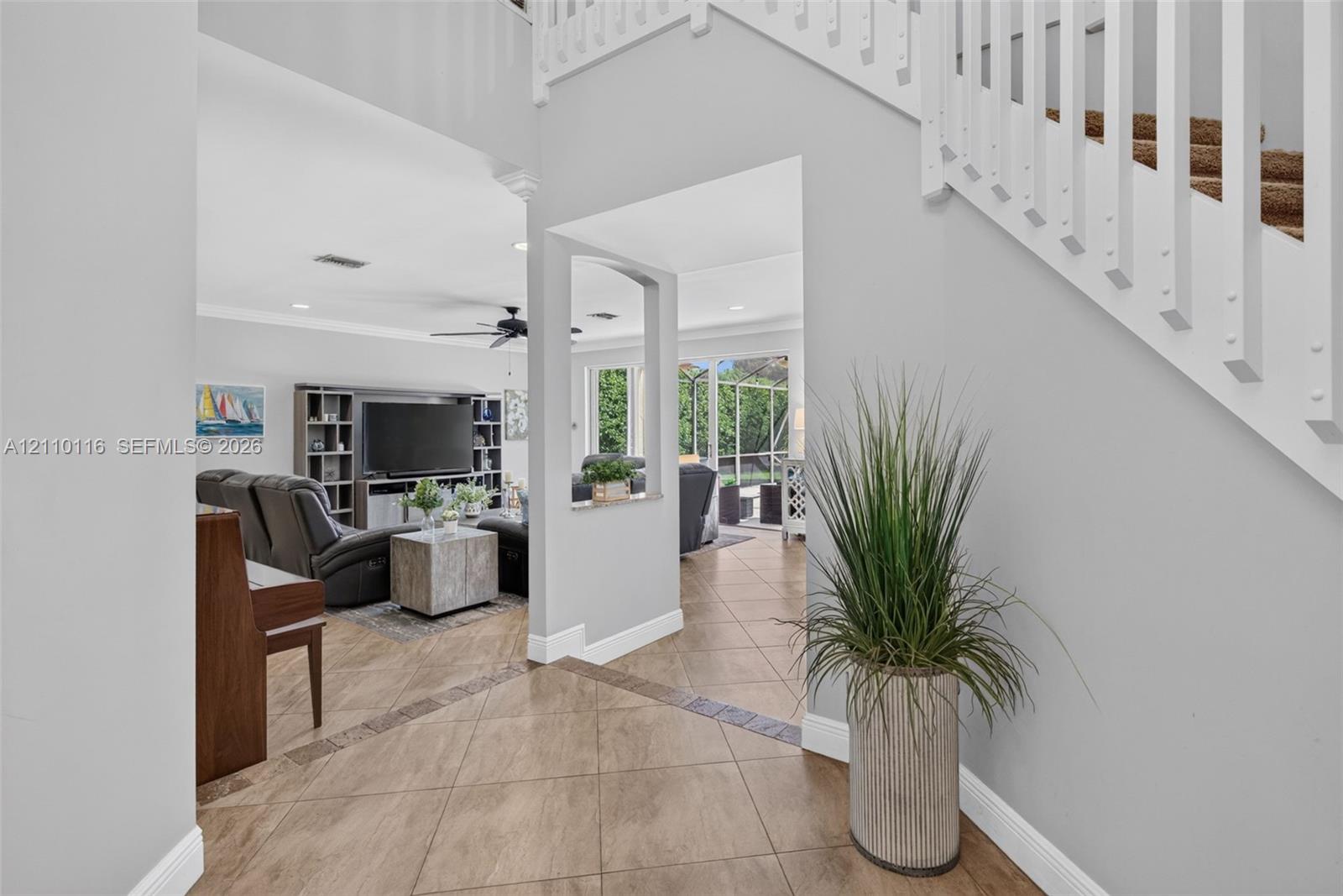 Two-story foyer featuring tile flooring with decorative inlay, a staircase with white balusters, and a pass-through window opening to the living area Two-story foyer featuring tile flooring with decorative inlay, a staircase with white balusters, and a pass-through window opening to the living area