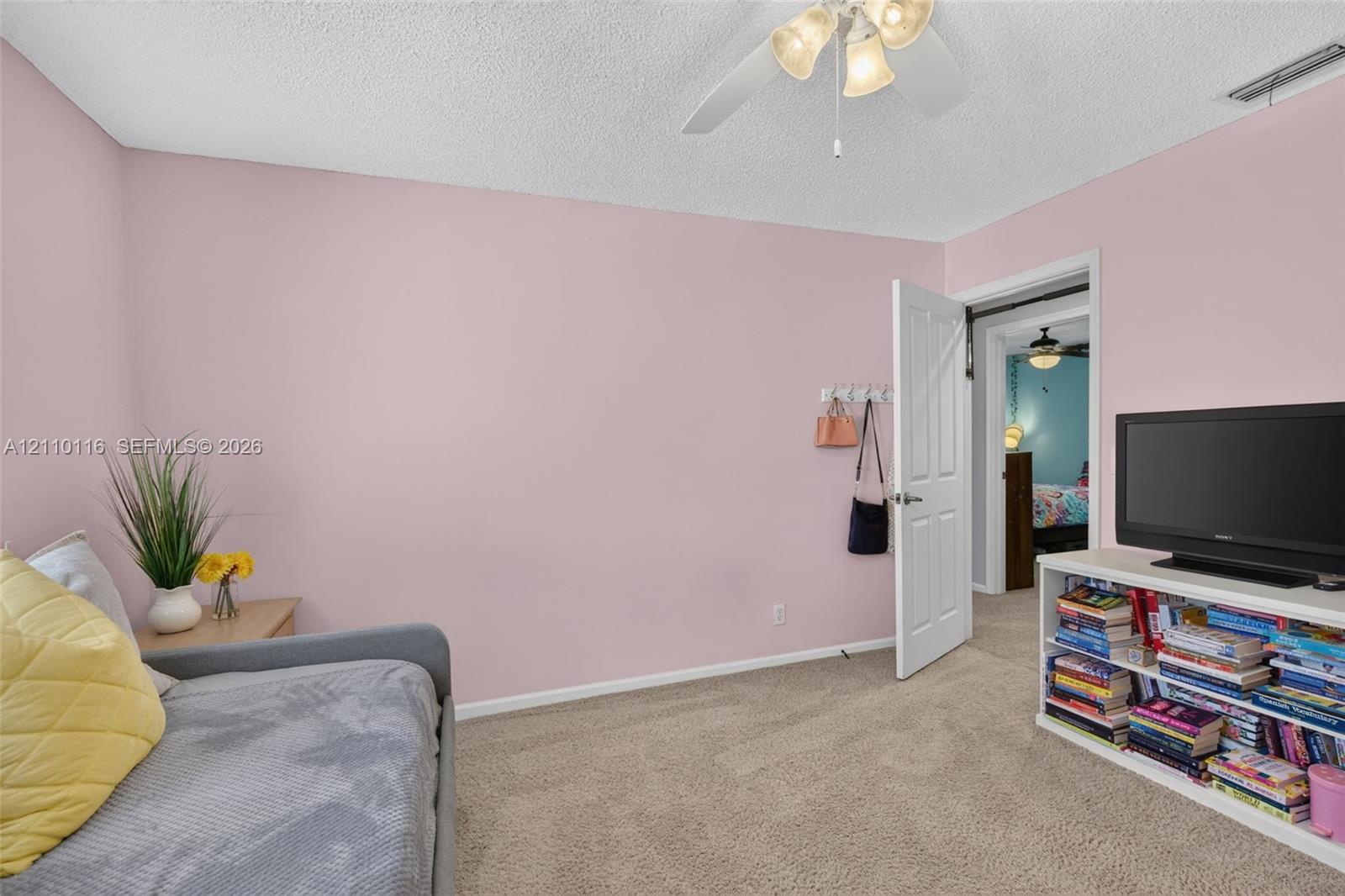 Interior space featuring neutral carpeting, a textured ceiling, a four-blade ceiling fan with integrated lighting, and a six-panel interior door