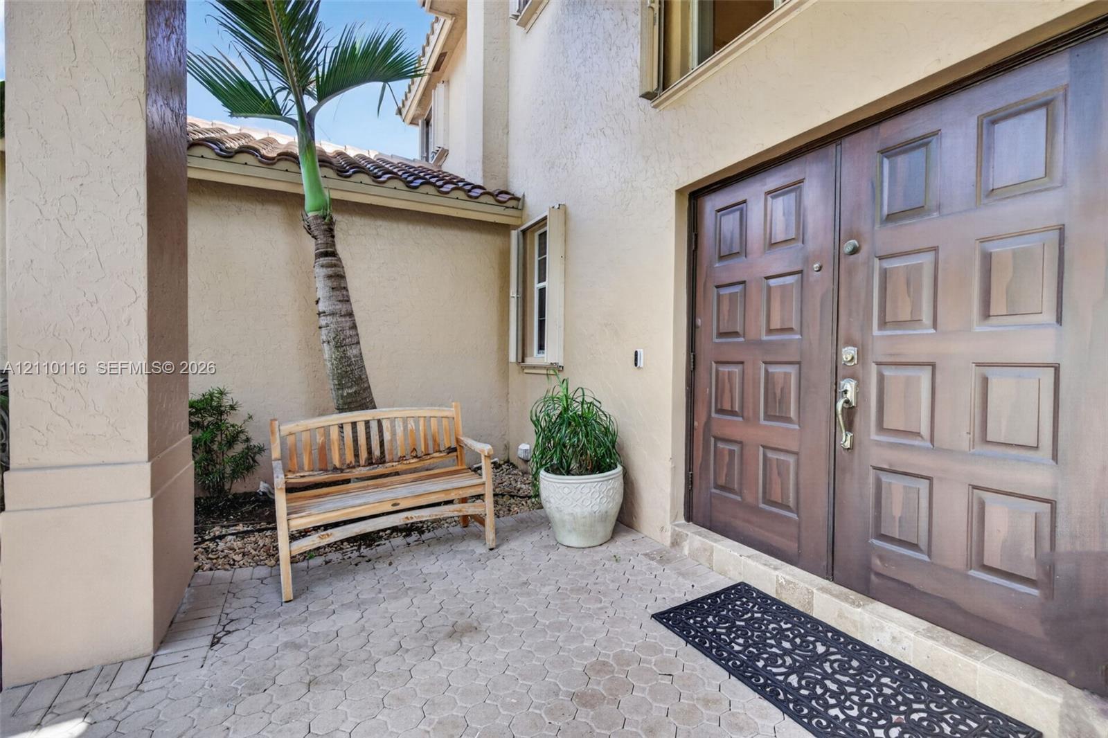 Stucco exterior entrance featuring a double-door entry with raised panel detailing, concrete paver flooring, and a tiled roofline