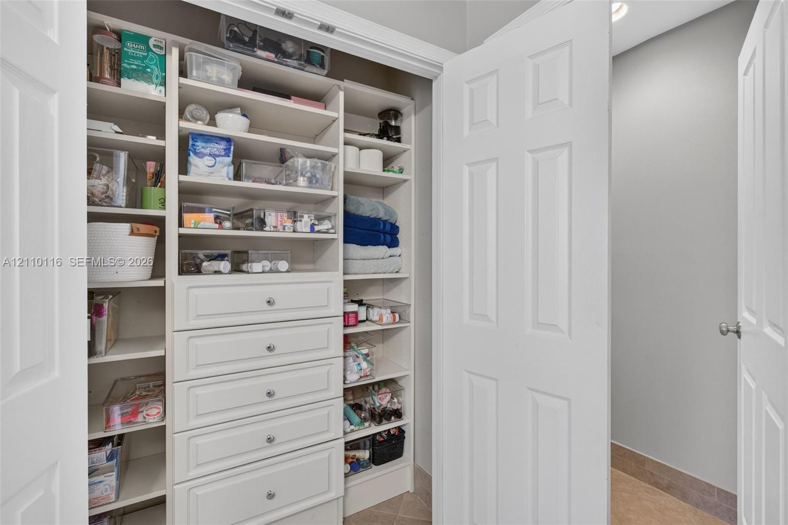 Linen closet featuring white built-in shelving, integrated drawers with metallic hardware, and double-door entry