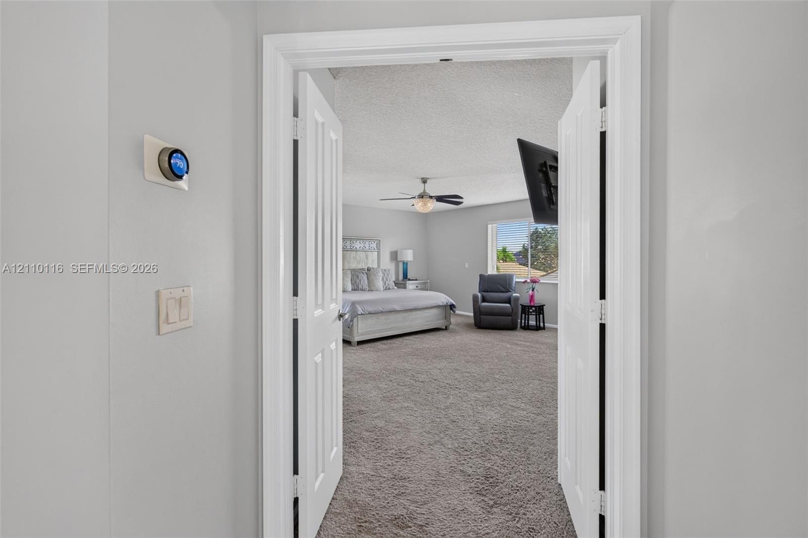 Double door entrance featuring wall-mounted smart thermostat, carpeted flooring, ceiling fan with integrated lighting, and dual-pane window