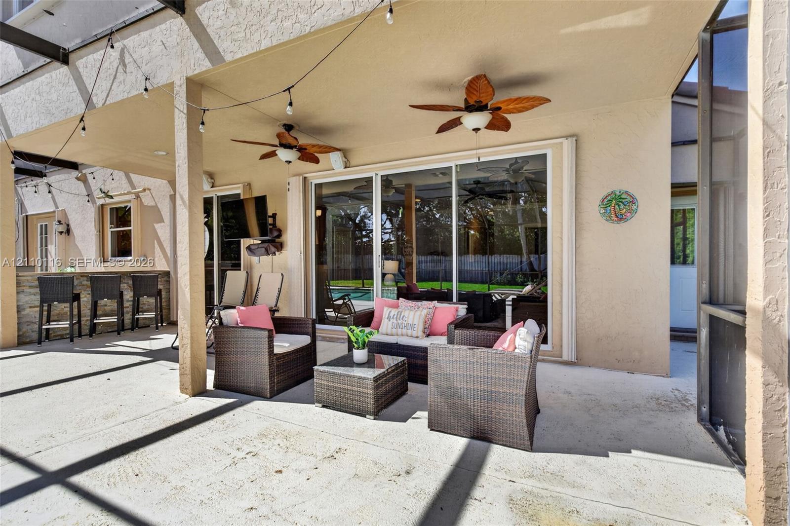 Covered outdoor living area featuring a concrete patio, stone-veneer wet bar, dual ceiling fans, and sliding glass entry doors