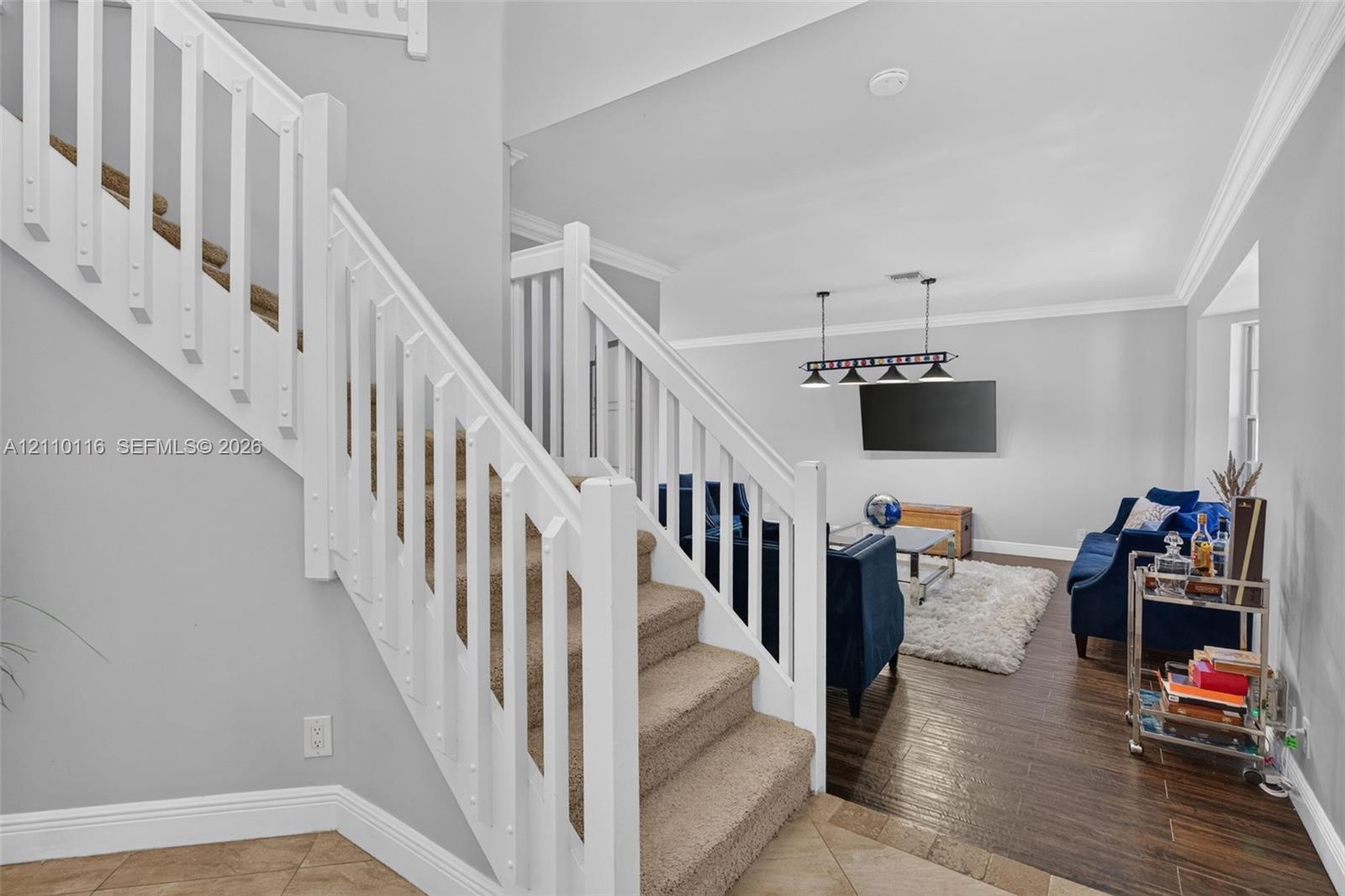 Staircase featuring white balusters and handrail, neutral-tone carpeting, wood-finish flooring, and crown molding Staircase featuring white balusters and handrail, neutral-tone carpeting, wood-finish flooring, and crown molding