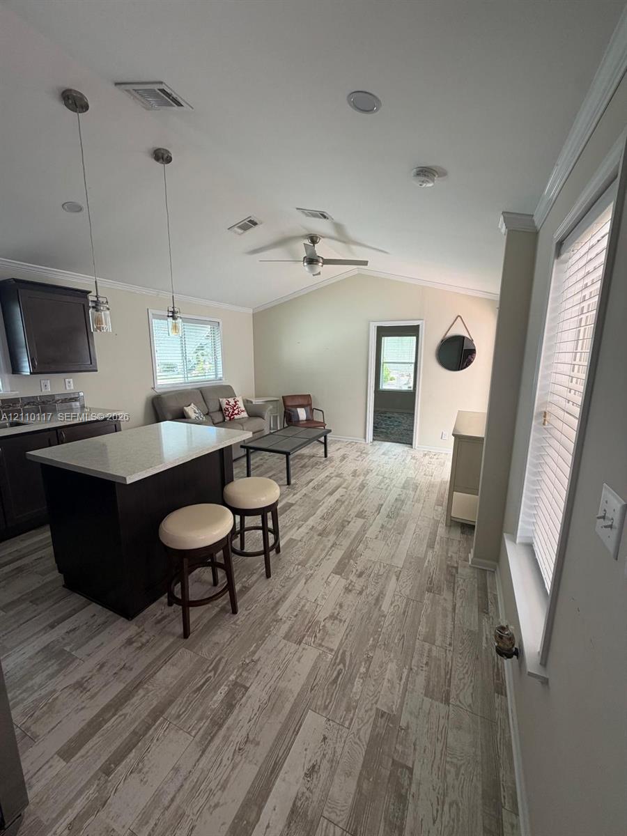 Open-concept interior featuring vaulted ceilings, wood-finish flooring, a central island with a stone-composite countertop, dark wood cabinetry, and recessed lighting