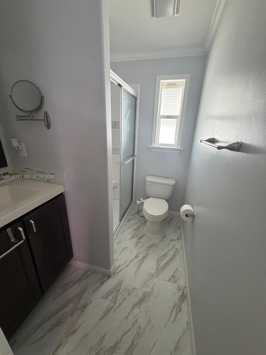Bathroom featuring dark wood-finish cabinetry, a white molded vanity countertop, shower enclosure with glass doors, and patterned tile flooring