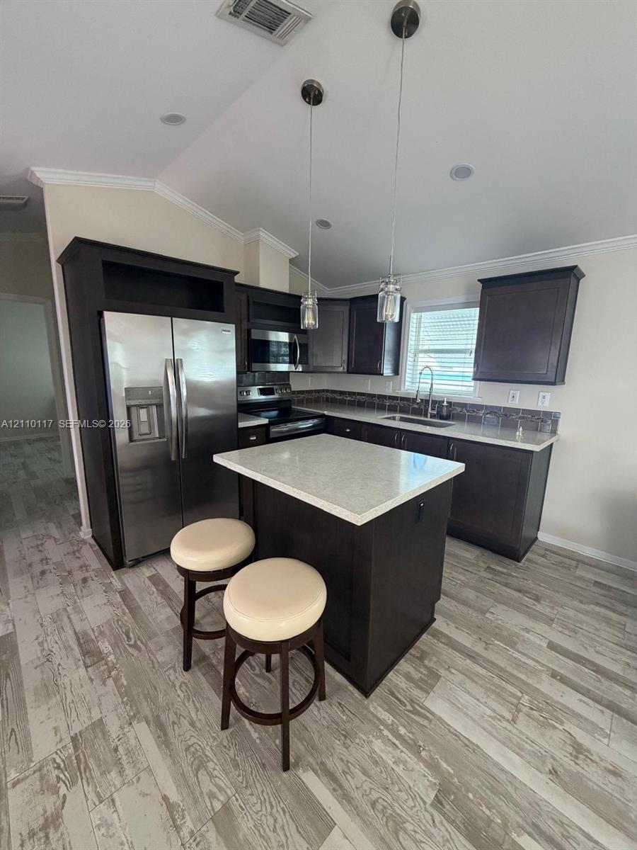 Kitchen featuring dark cabinetry, stone-finish countertops, stainless steel appliances, a center island, and wood-finish flooring
