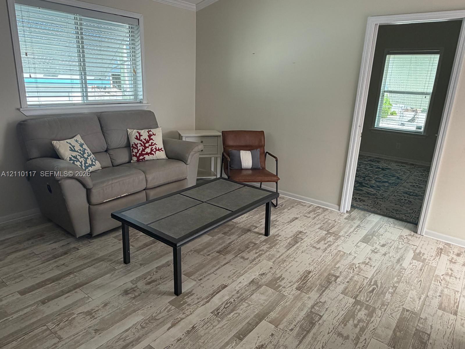 Wood-finish flooring, neutral wall tones, crown molding, and horizontal slat window blinds