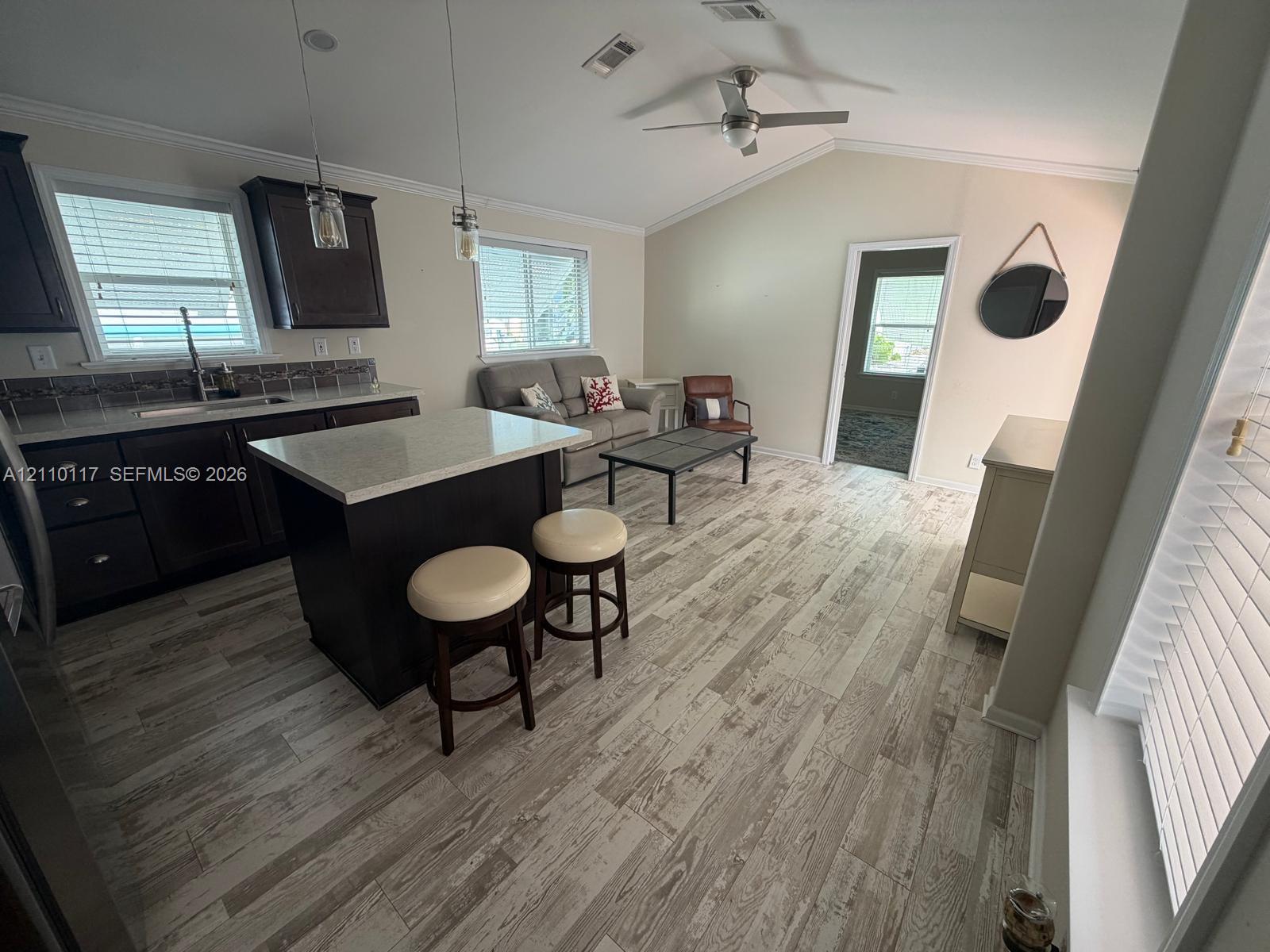 Kitchen featuring dark cabinetry, quartz countertops, a central island with bar seating, vaulted ceilings, and wood-finish flooring