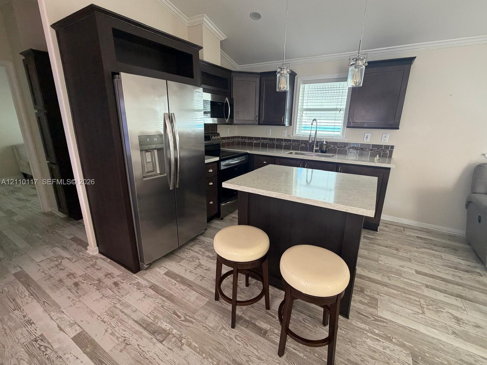 Kitchen featuring dark-finish cabinetry, a center island with a stone-composite countertop, wood-finish flooring, stainless steel appliances, and glass pendant lighting