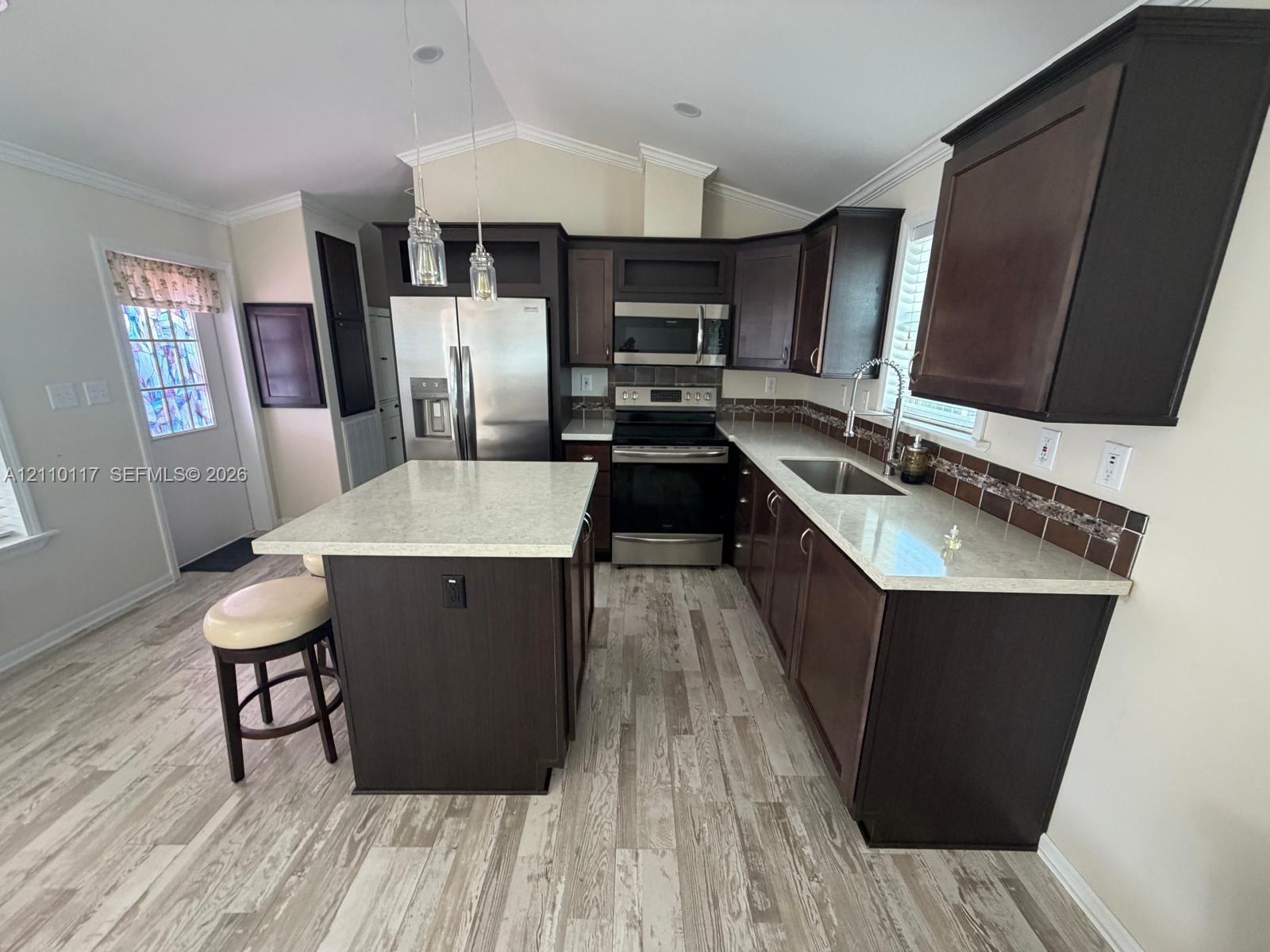Kitchen featuring dark-finish cabinetry, an island with stone-surface countertop, stainless steel appliances, tile backsplash, and wood-finish flooring