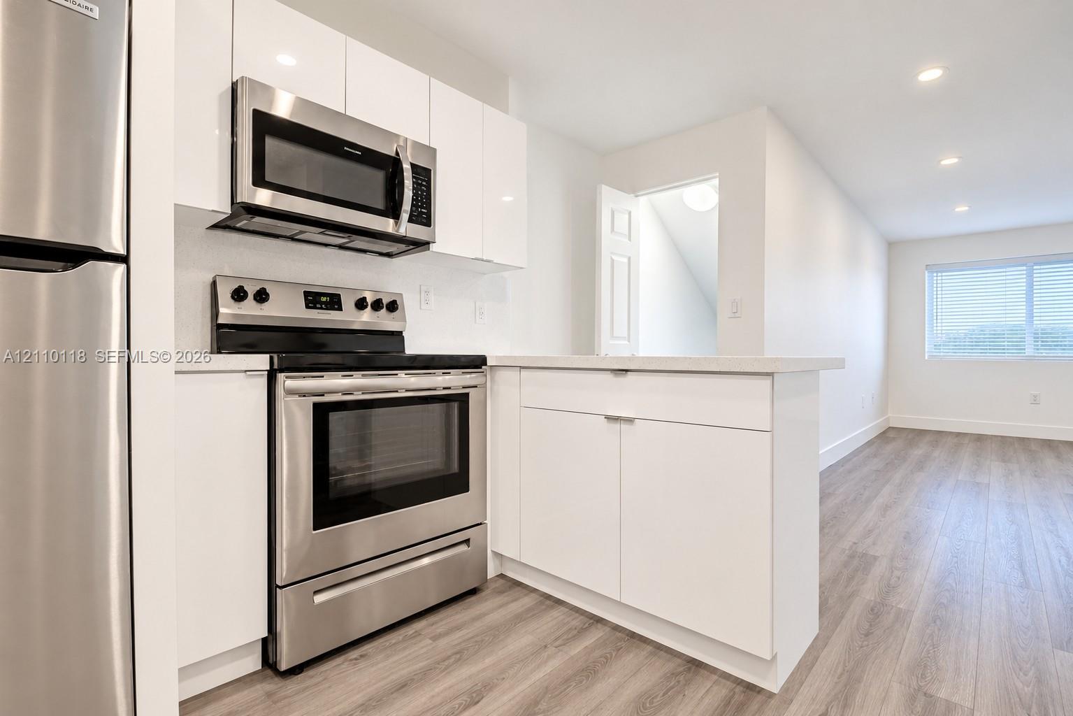 Kitchen featuring white flat-panel cabinetry, stainless steel appliances, solid-surface countertops, and wood-finish flooring with recessed lighting