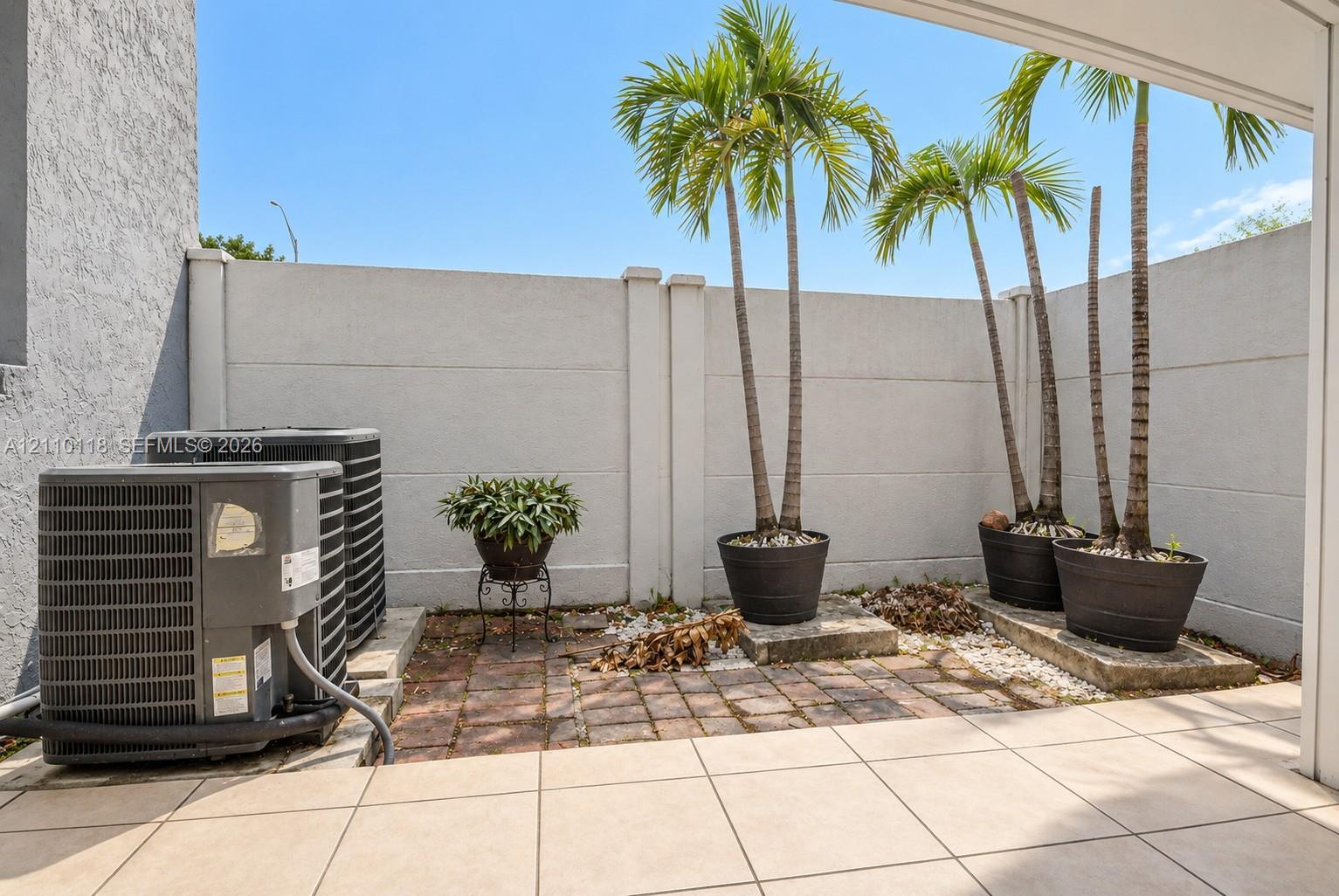 Private outdoor patio featuring large-format tile flooring, a structured masonry privacy wall, and brick paver accents