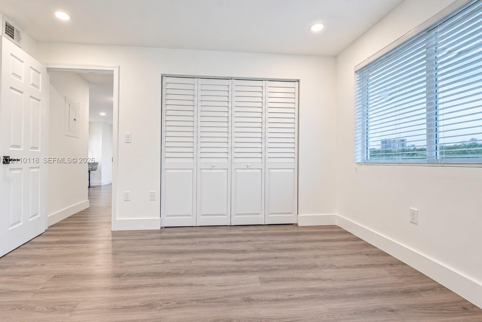 Room featuring wood-finish flooring, recessed lighting, four-panel louvered closet doors, and a window with horizontal blinds