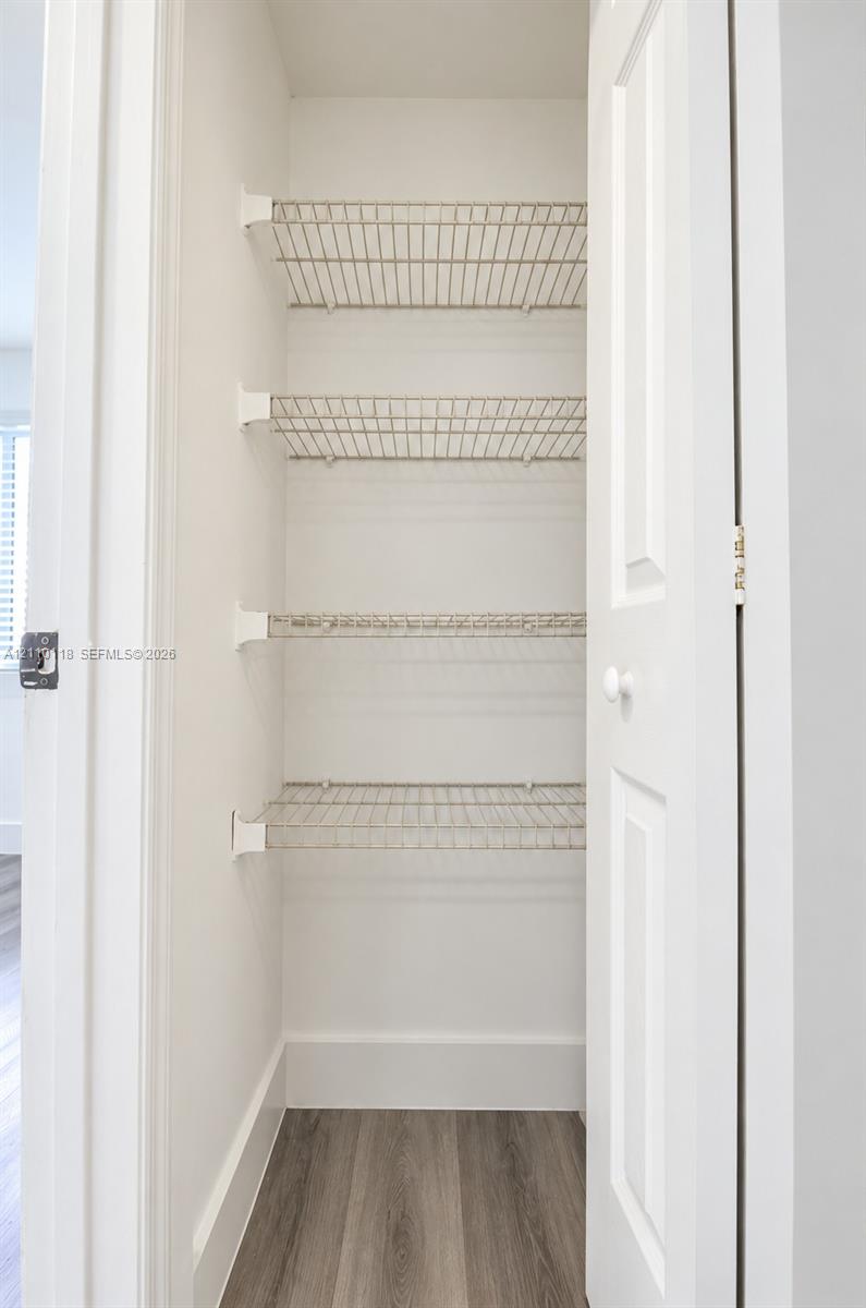 Storage closet featuring white-painted walls, four tiers of wire shelving, and wood-finish flooring