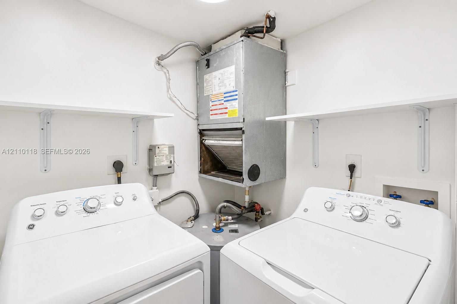 Utility space featuring a wall-mounted air handler, a water heater, dual wall-mounted shelving units, and dedicated hookups for laundry appliances