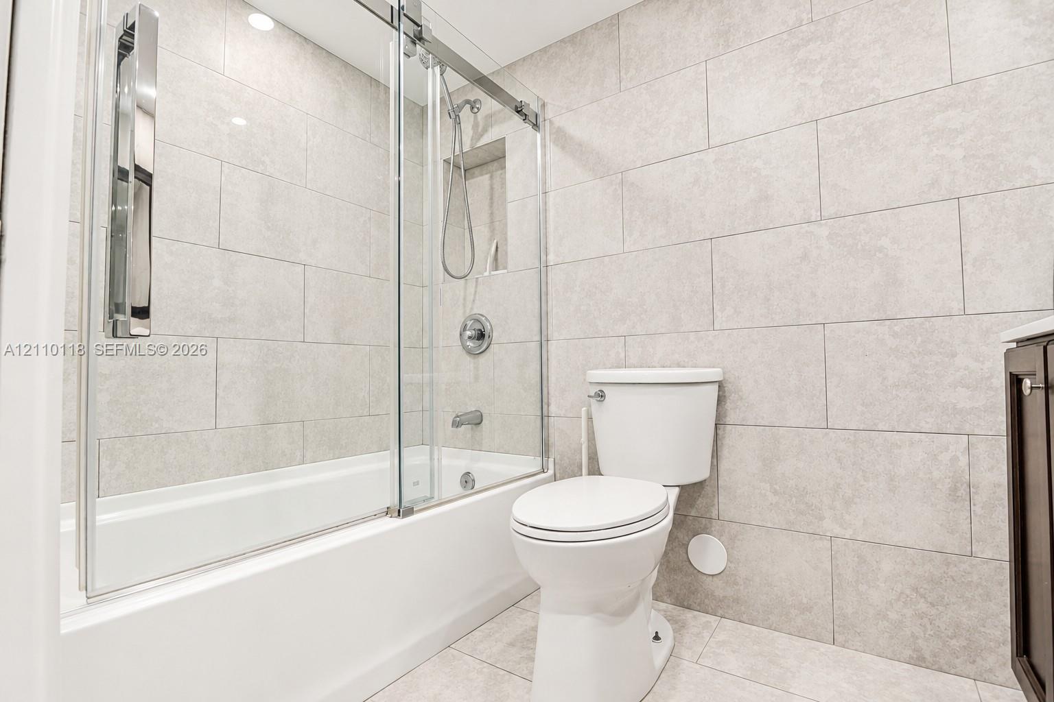 Full-height wall tiling, glass sliding shower enclosure, recessed shower niche, tub-shower combination, and polished chrome fixtures